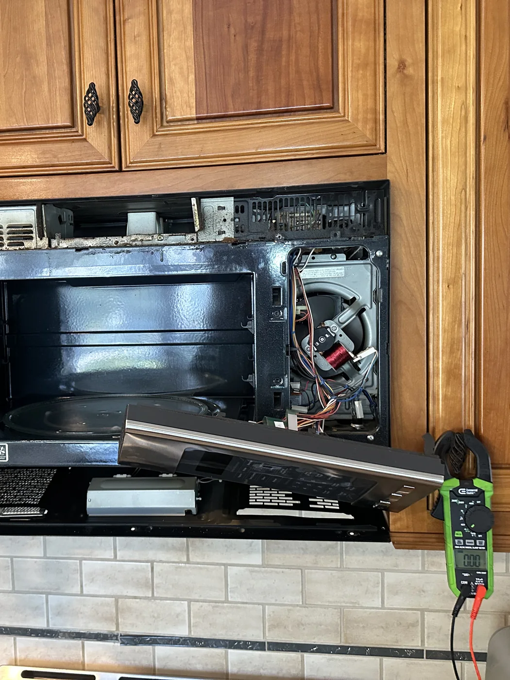GE microwave with panel removed for diagnostics with a clamp meter